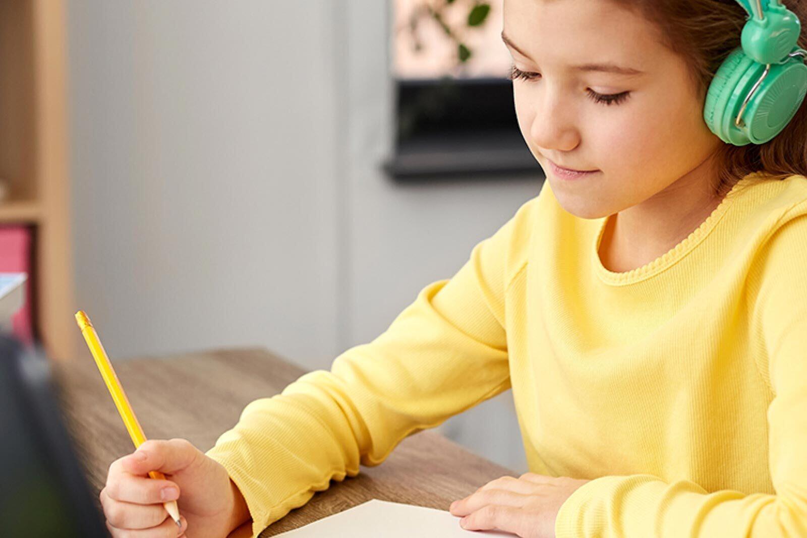 A child is studying at a desk with her headphones on.